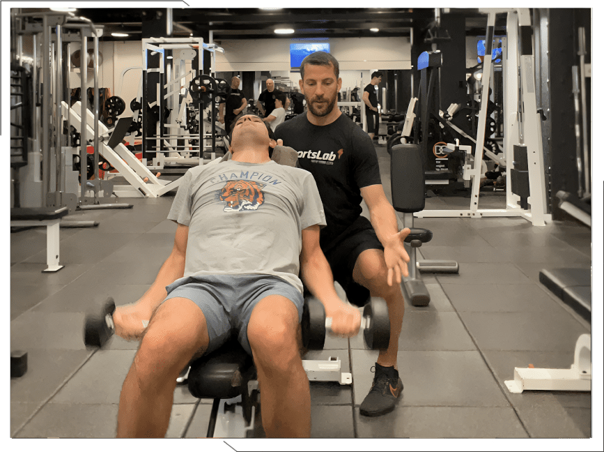 Man lifting dumbbells with trainer in gym.