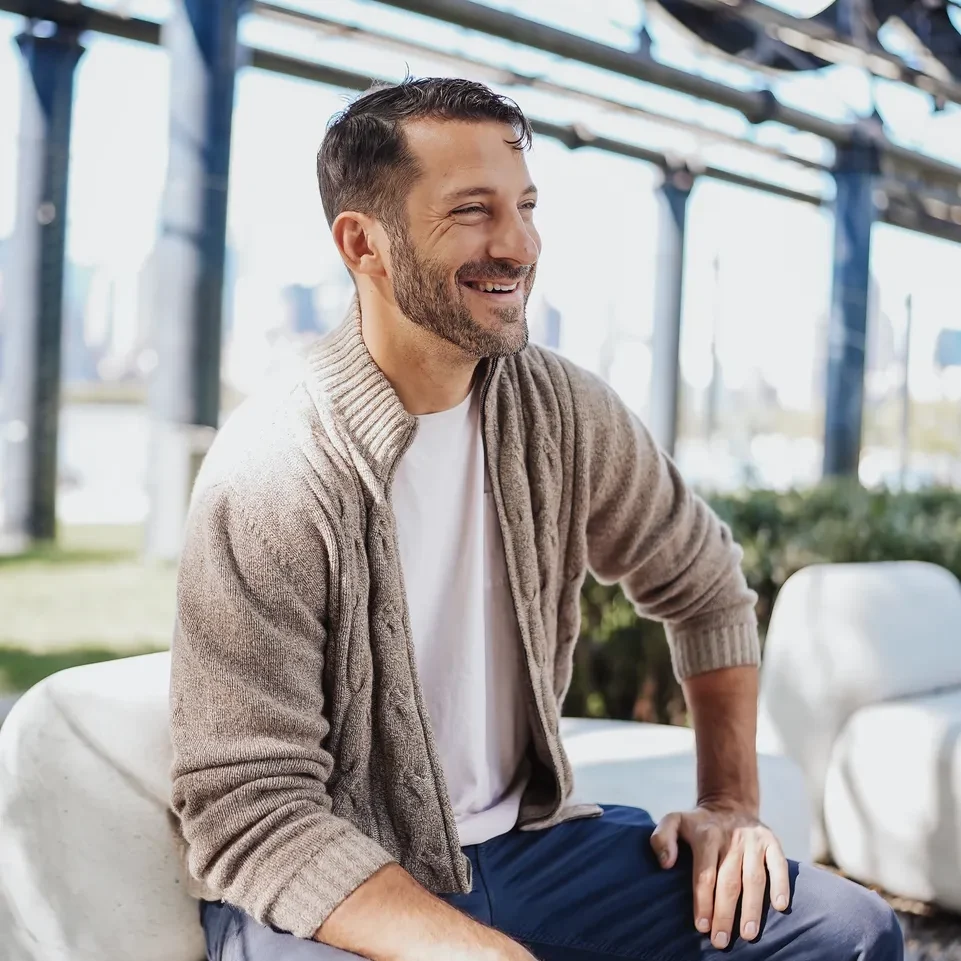 Happy man with a beard sitting indoors, smiling and relaxed.